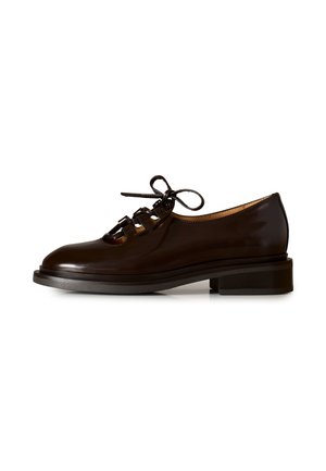 Scarpa in pelle marrone scuro con tacco basso, dettagli ritagliati e lacci anteriori annodati, mostrata su sfondo bianco.