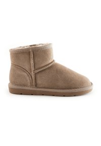 Botte de cheville en suède beige avec une doublure douce, un bout rond et une semelle en caoutchouc plate. Présente des détails cousus et un dessus retroussé.