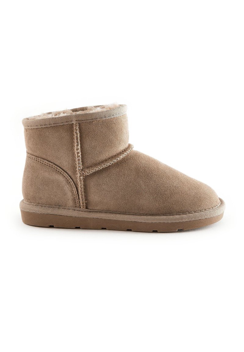 Botte de cheville en suède beige avec une doublure douce, un bout rond et une semelle en caoutchouc plate. Présente des détails cousus et un dessus retroussé.