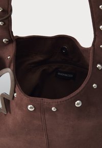 Sac fourre-tout en daim marron avec des clous en argent le long du bord, une poche zippée à l'intérieur, et une étiquette portant le nom de la marque "even&odd."