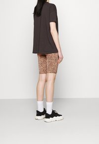 Dark oversized t-shirt, paired with pink leopard print bike shorts. Black sneakers with white soles and white socks. Minimalist background.