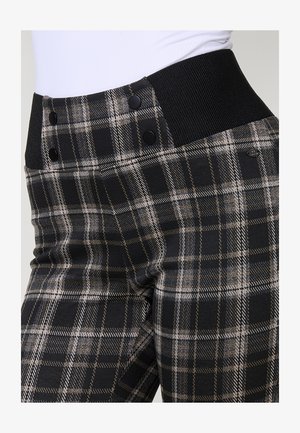 I pantaloni a quadri neri e grigi presentano un alto punto vita con tessuto nero a coste, due grandi bottoni neri e sottili dettagli in filo dorato.