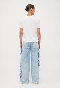 T-shirt blanc à manches courtes associé à un pantalon cargo large bleu clair avec de multiples poches latérales et une texture semblable au denim.