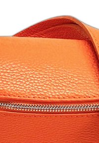 Oranje gestructureerde synthetische leren tas met een zilveren rits en band, met een gladde bovenkant en gebogen lijnen.