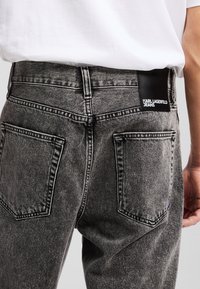 Sive traperice s izblijedjelom teksturom, koje imaju kožni tag s natpisom "KARL LAGERFELD JEANS" i dva stražnja džepa s kontrastnim šavovima.