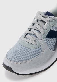 Grey mesh and suede athletic shoe featuring a textured finish, round toe, padded tongue, and contrasting dark accents on the sides.