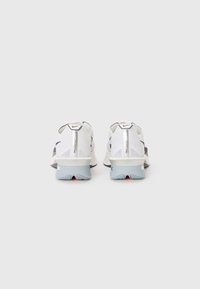 Sneakers with a white mesh upper, dark accents, reflective details, and a light blue sole featuring red accents. Back view displays logo.