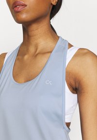 Débardeur de sport bleu clair en tissu lisse, avec de larges bretelles et un col rond. Comprend un petit logo blanc sur la poitrine.