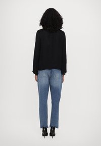 Svart langermet topp med teksturert detaljer, kombinert med lyseblå denimjeans med en avslappet passform og subtil blekning. Svart ankelboots med hæl.