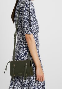 Borsa a tracolla in pelle verde oliva con due scomparti con zip, dettagli con nappina e tracolla regolabile.