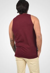Burgundy ujjatlan trikó, pamutból készült, laza szabással és sima textúrával, bézs nadrággal viselve.