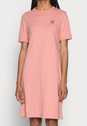 Femme portant une robe rose à manches courtes, longueur genou, avec un petit logo d'oiseau jaune sur la poitrine gauche.