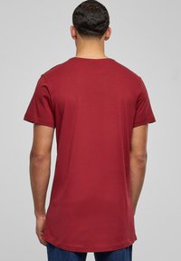Bordo majica kratkih rukava s okruglim izrezom, izrađena od glatkog materijala, s laganim, širokim krojem i malo produženim stražnjim rubom.