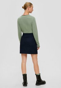 Helles grün langärmliges Oberteil, kombiniert mit einem dunkelblauen gestreiften Rock, schwarzen Stiefeln und grünen Socken. Einfaches und figurbetontes Design.