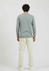 Lichtgrijze crewneck trui gemaakt van een zachte, gestructureerde brei, gecombineerd met off-white broek en witte sneakers, gezien vanaf de achterkant.