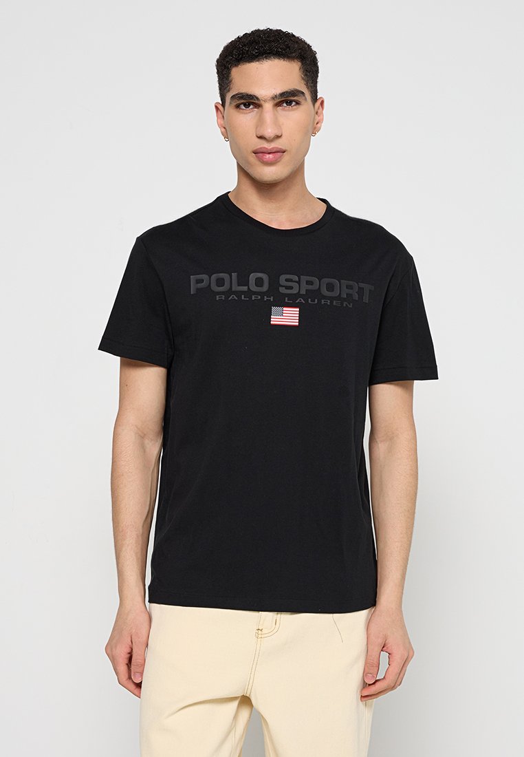 T-shirt in cotone nero con la scritta "POLO SPORT" e "RALPH LAUREN" in lettere maiuscole, e un piccolo dettaglio della bandiera americana sul petto. Maniche corte.