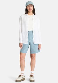Leichte weiße Leinenhemd, hellblaue Baumwollshorts und beiges Schuhwerk mit dicken Sohlen. Passende hellblaue Kappe, einfaches Design.