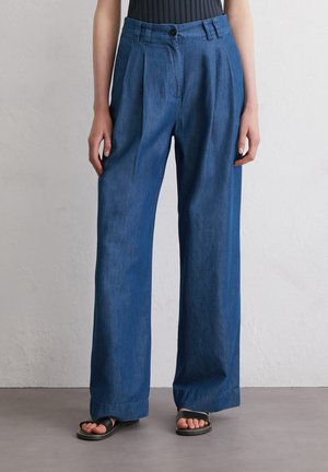 Jeansweite Hosen in Dunkelblau mit hoher Taille, gefältelter Vorderseite und lässigem Schnitt. Getragen mit schwarzen minimalistischen Sandalen.