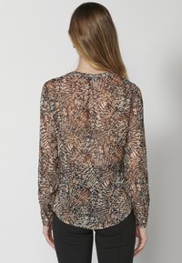 Blusa trasparente a maniche lunghe con motivo di foglie di palma marroni e crema, scollatura rotonda e dettagli con polsini abbottonati.