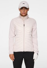 Ljusrosa zip-up-jacka med vadderad framdel och jerseyärmar, utrustad med hög krage och blixtlåsförsedda sidofickor. Vit keps och handske ingår.