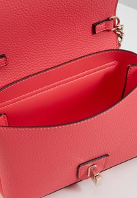 Borsa a tracolla in pelle rosa con texture, dotata di un interno liscio, chiusura magnetica e dettagli di cucitura discreti. Vista aperta che mostra i compartimenti interni.
