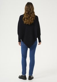 Musta neuleponcho, jossa on salmiakkikuvio ja vinomallinen helma. Yhdistettynä sinisiin skinny-farkkuihin ja mustiin platform-kengiin.