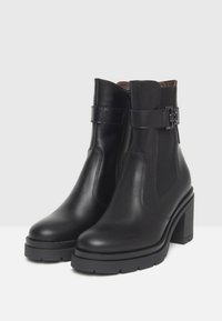 Black leather ankle boots with chunky heels, side elastic panels, zipper closure, and decorative buckle straps.