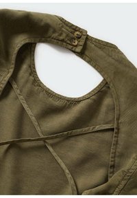 Vêtement vert olive avec un col rond et deux boutons marron à l’arrière, comportant des détails de couture et des bretelles en tissu.