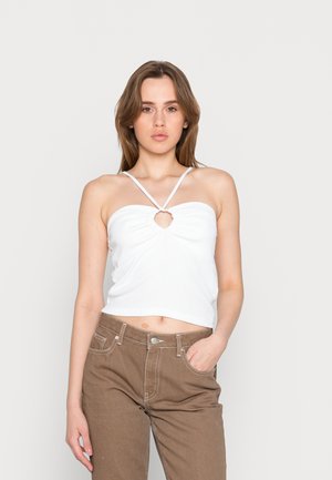 Top cropped branco canelado com detalhe de buraco e alças finas, combinado com calças castanhas de cintura alta com costuras em contraste e pockets.