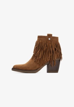 Stivaletto in suede marrone con dettagli in frange, punta arrotondata e tacco in legno impilato. Dettaglio a bottone alla caviglia.