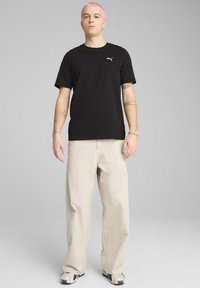 Sort bomulds T-shirt med korte ærmer og et lille Puma-logo. Matchet med beige, løstsiddende bukser og sorte og hvide sneakers.