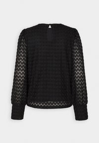 Haut noir à manches longues avec un tissu texturé et à motif, présentant un détail de dos en forme de trou de clé et un col arrondi.