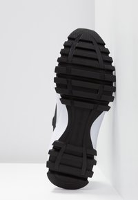 Black and white sneaker featuring a textured rubber sole with deep grooves and a smooth upper for optimal grip and support.