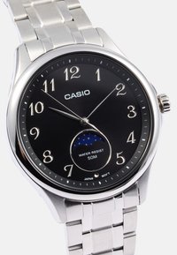 Reloj de pulsera Casio con esfera negra, números plateados, pulsera de acero inoxidable, indicador de fase lunar y resistencia al agua de hasta 50 metros.