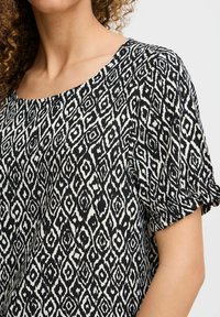 Top a righe bianco e nero con un design geometrico, scollo a barca ampio e maniche corte a sbuffo con dettagli in elastico.