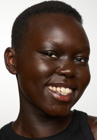 Zbliżenie osoby o ciemnej karnacji, krótkich włosach i szerokim uśmiechu. Wyróżniające cechy to gładka skóra, widoczne zęby i czarna bluzka.