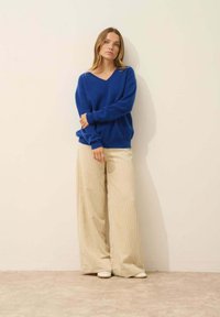 Blå v-ringad tröja i kombination med vida, ribbade beige byxor. Tröjan har en avslappnad passform; byxorna har vertikal struktur och en fladdrande siluett.