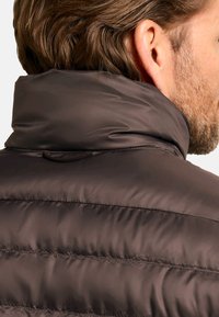 Dark brown puffer jacket with a high collar, matte finish, and horizontal quilted pattern. Includes a small loop detail at the back.