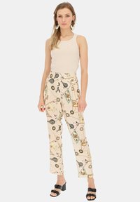 Jasnobeżowe spodnie w nadruki z motywami marynistycznymi mają luźny krój i wysoki stan. Zestawione z dopasowanym kremowym topem na ramiączkach.