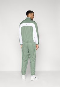 Πράσινο και λευκό φόρμα με τζάκετ με φερμουάρ και παντελόνια με ελαστική μέση. Ελαφρύ ύφασμα με λογότυπο στην πλάτη και ριμπ μανσέτες.