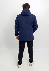 Giacca blu navy con cappuccio, finitura liscia e design trapuntato. Abbinata a pantaloni scuri e sneakers bianche.