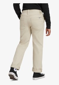 Beige Baumwollmischhosen mit geradem Bein, aufgerollten Bündchen und Gesäßtaschen, getragen mit schwarzen High-Top-Sneakern.