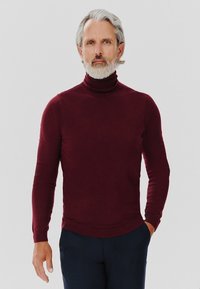 Bordowy sweter typu golf wykrojony z miękkiego materiału, z długimi rękawami i dopasowanym krojem, zestawiony z ciemnymi spodniami.