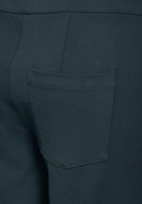Dunkelblaugrüne Hose mit glatter Textur und einer einzigen Gesäßtasche, ausgestattet mit sauberer Naht und rechteckiger Form.