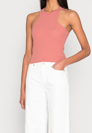 Top a coste senza maniche in rosa polveroso, caratterizzato da un colletto alto e aperture laterali, abbinato a pantaloni bianchi a vita alta e a gamba larga.