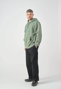 Light green hoodie with a front pocket and hood. Black pants and dark shoes complete the outfit. Simple, casual design with no patterns.