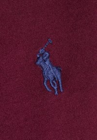 Burgundytyg med en subtil, slät textur som har en framträdande blå broderad polo-spelare logo, placerad på vänster sida.