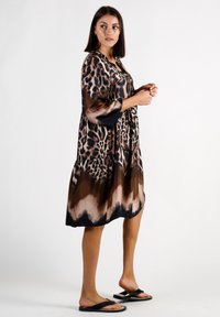 Leopardenmusterkleid mit fließender Silhouette, das braune und schwarze Farbtöne zeigt. Aus leichtem Stoff gefertigt, mit drei Viertel langen Ärmeln und einem gestuften Saum.