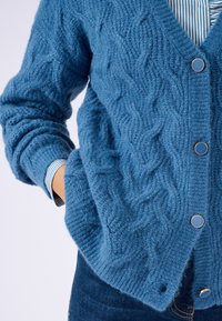 Cardigan blu a maglia con motivo a treccia, dotato di scollo a V e cinque bottoni. Tessuto strutturato, con polsini e orlo a costine.