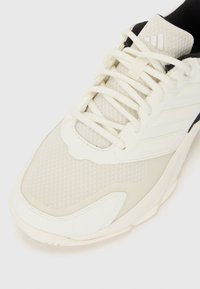 Weißer Sportschuh mit einem strukturierten Mesh-Obermaterial, gepolstertem Knöchelbereich und schwarzen Akzenten. Ausgestattet mit beigen Schnürsenkeln und einer leicht geschwungenen Gummisohle.